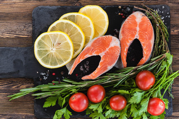 Two salmon steakes with greenery, lemon and cherry tomatoes on the black board