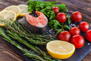 a salmon steak with greenery, lemon and cherry tomatoes on the black board