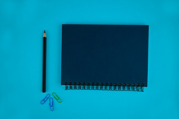 Three different colored paper clips,a black pencil crayon,and a diary on a blue background