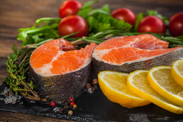Two salmon steakes with greenery, lemon and cherry tomatoes on the black board