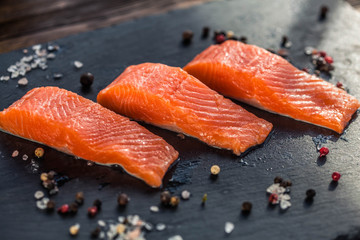 Three salmon steakes with thyme, rosemary, pepper and salt grains on the black board