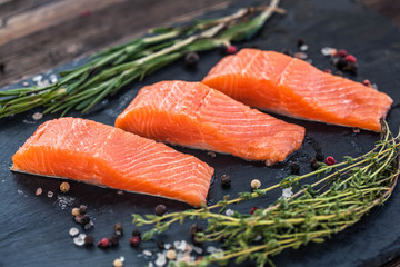 Three salmon steakes with thyme, rosemary, pepper and salt grains on the black board