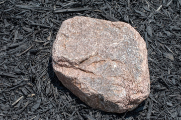 A large flat rock fills space in the garden surrounded by black mulch in Missouri. Bokeh effect.