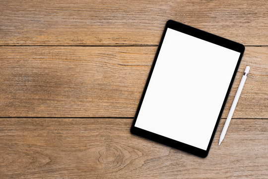 Mockup image of black tablet computer pc with blank white screen with pencil isolated on wood table background. up high view.