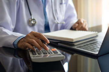 Doctor using calculation machine at office desk.