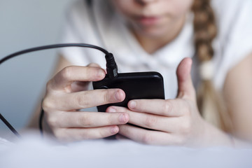 teen girl listening to music from a smartphone with headphones and sitting at home in quarantine, coronavirus, entertainment concept
