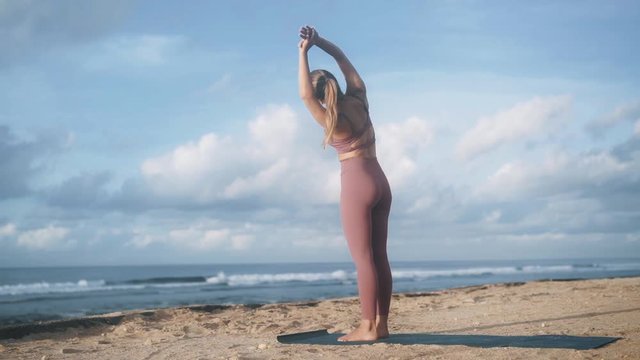 slim woman standing on ocean beach does half moon yoga pose