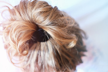 Naklejka premium messy bun on the head of a blonde woman. slightly curly hair. Modern fast hairstyle messy hair. bad hair day concept. quick hairdo at home. 