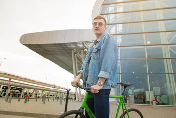 A guy in a blue denim jacket on green bicycle. Man on the background of the city on a bike.