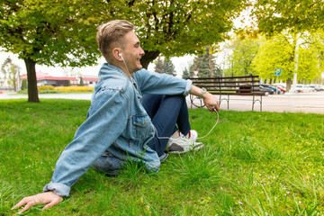 Fototapeta premium A young man listens to music on headphones. The guy sitting on the grass.