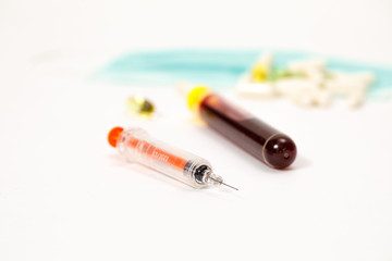 syringe for injection and test tube with blood, pills on a white background