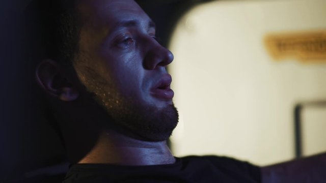Muscular strong man doing pec deck butterflies and looking forward while exercising on fitness machine. Healthy athlete at the dark night gym in slow motion. Close up. 50 fps