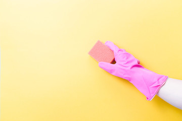 hand in pink rubber glove holds orange sponge for washing dishes and cleaning, yellow background copy space, cleaning concept