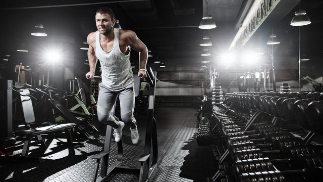 Muscular bodybuilder working out in gym doing exercises on parallel bars. 