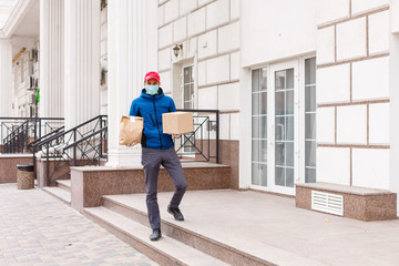 Fototapeta premium Courier in protective mask and medical gloves delivers takeaway food. Delivery service under quarantine, disease outbreak, coronavirus covid-19 pandemic conditions.