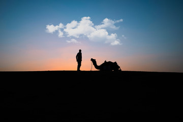 silhouette of an adult and camel on the sand dunes at sunset