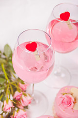 Two glasses with pink grape wine with clothpin heart shaped and roses on the background. Romantic dinner concept.