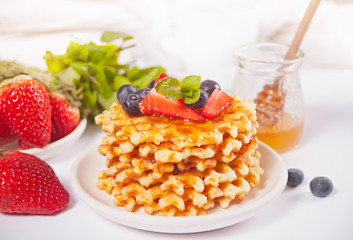 Plate with sweet tasty waffles with honey, berries, cup of tea on the white background.