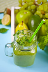 Fresh blended green smoothie in glass jar with fruit and vegetables on the background. Health and detox concept.