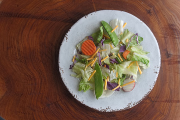 Mixed salad on a white plate on a cross section of a tree trunk with rings