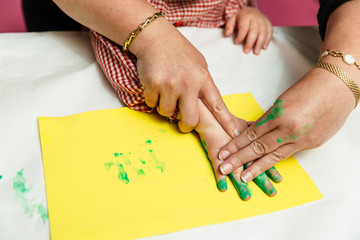 las manos de una mujer cogen la mano de un niño de 5 años con bata escolar para pintar con la...
