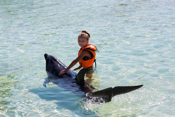 little girl hugging and swimming with bottlenose dolphins in blue water. © viclin