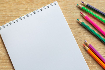 Notepad and colorful pencils on a wooden table. Top view