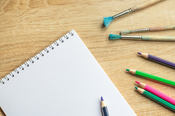 Notebook and colorful pencils on a wooden table. Top view