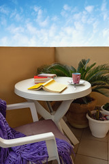 Spending time at home. Books and cup of coffee on white table on small balcony