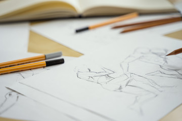 A top view flat lay of many figure drawing pencil and marker sketches. The artist worskspace with male and female drawings and pencils on the white paper, art, craft, creativity, inspiration, concepts