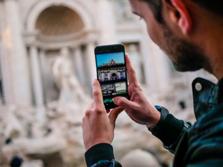Junger Mann mit Smartphone fotographiert den Trevi Brunnen in Rom