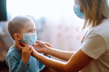 Little boy and mom in medical mask. Mother puts on her baby sterile medical mask. Child, wearing...