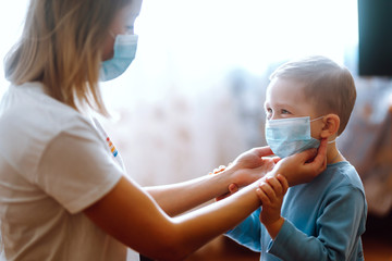 Little boy and mom in medical mask. Mother puts on her baby sterile medical mask. Child, wearing...