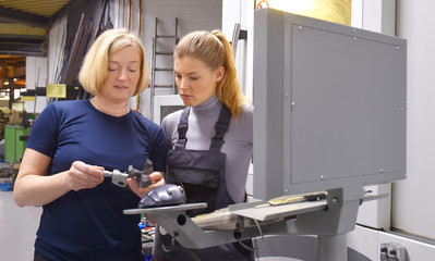 A young trainee receives tuition from her trainer. Both women work as computerized  numerical control engineers. They are seen  together at their high tech place of work.