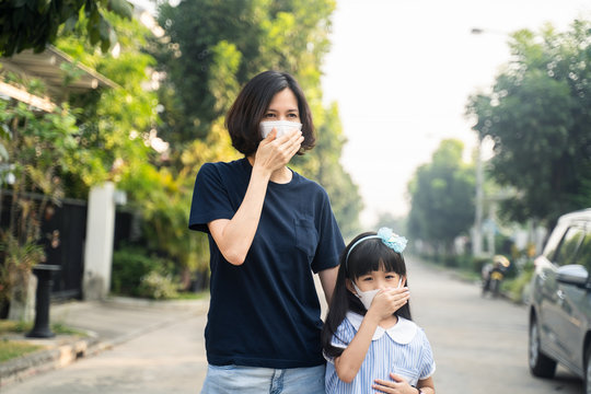 Asian mother woman and little young girl daughter wearing mask for prevent Covid-19 or Coronavirus amd dusk pm 2.5 air pollution. Kid and mom cough due to bad smell and allergic symptom on street.