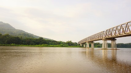 A view on the river bank and a long bridge over the river. Visible mountains across the river.