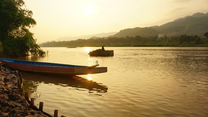 The view on the edge of a lake in the morning. A canoe and mountains were seen across the lake.