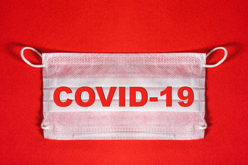 Medical white mask on a red background with the words COVID -19. Concept of coronavirus, epidemic quarantine and influenza virus. Minimal virus protection concept