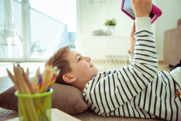 Teen boy lying on the floor and having online video call with friends during coronavirus quarantine
