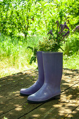 a pair of rubber boots with a bouquet of flowers stand on wooden boards on the street