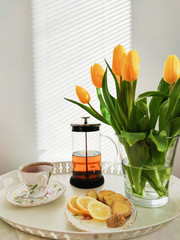 Plate of tea, lemon and ginger on bed table with yellow tulips