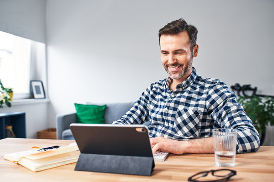 Smiling man working at a desk from home using digital tablet