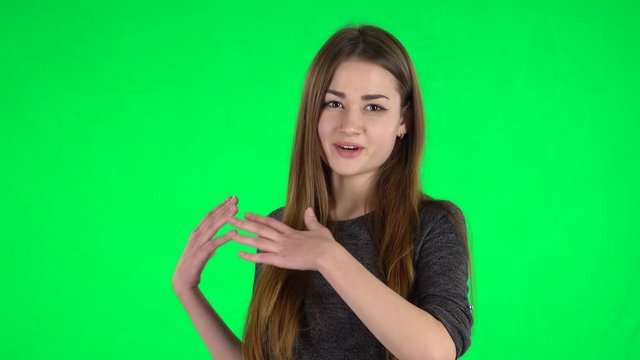 Portrait of cute brunette with long hair is waving hand and showing gesture come here on a green screen