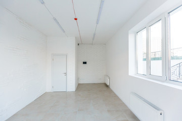 Fototapeta premium Light room with window and heating battery. Wall is of white plaster, has several outlets. Professional installation of electrical sockets, wires and switches. Connecting the light in flat or office