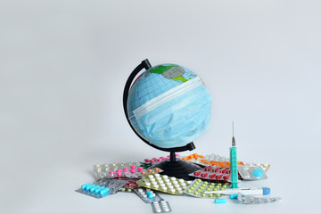 Obraz premium Globe in a medical mask against the background of pills.the globe is wearing a medical mask on white background. the inscription of a world pandemic. covid-19
