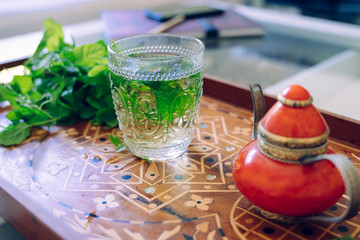 Detail of moroccan cold green herbal tea on a traditional tray. Healthy detox clear beverage. Arabian culture and traditions. Muslim lifestyle at home. Organic fresh moroccan hot infusion on a glass..