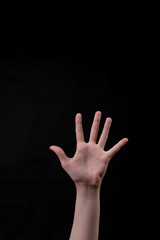 A hand on a black background. Beautiful girl's hand raised up. You can see all fingers. Minimalism