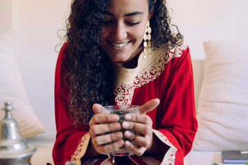 Beautiful young ethnic woman drinking herbal tea at home. Moroccan female with traditional clothes...