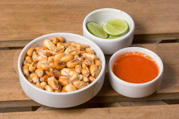 Toasted andean corn, lime slices and chili sauce served on white mini bowls