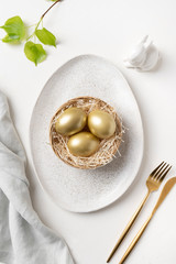 Easter table setting with bunny and golden eggs on white table. Top view.